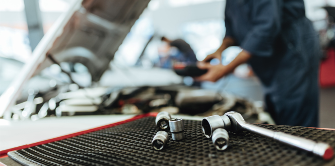 Close-up of socket wrench and fasteners with auto mechanic in the background